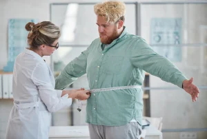 Bir doktor, obezite cerrahisi öncesinde hastasının bel ölçüsünü alıyor.